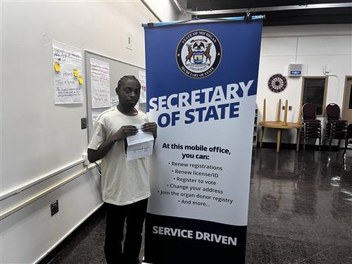 student standing next to Secretary of State banner holding documents